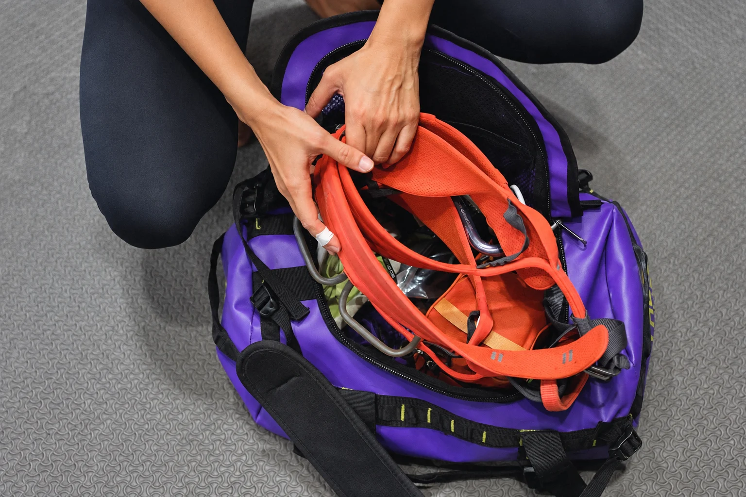 Open purple sports duffel with orange climbing gear and hands arranging contents