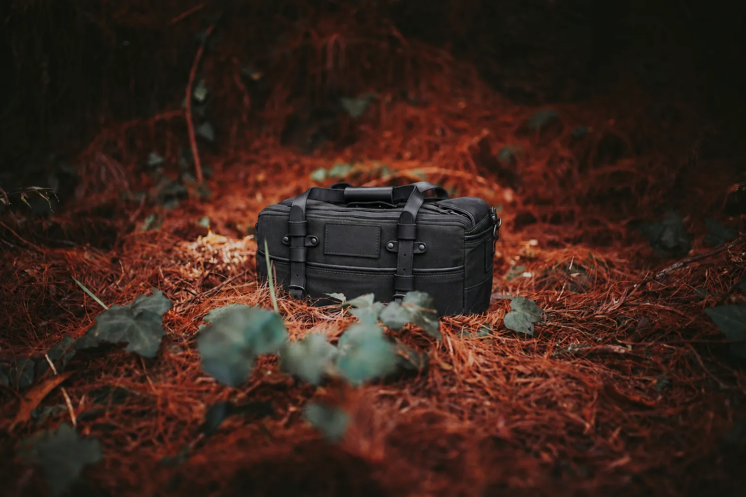 Charcoal duffel bag on a forest floor with stitched lower panels and handles visible