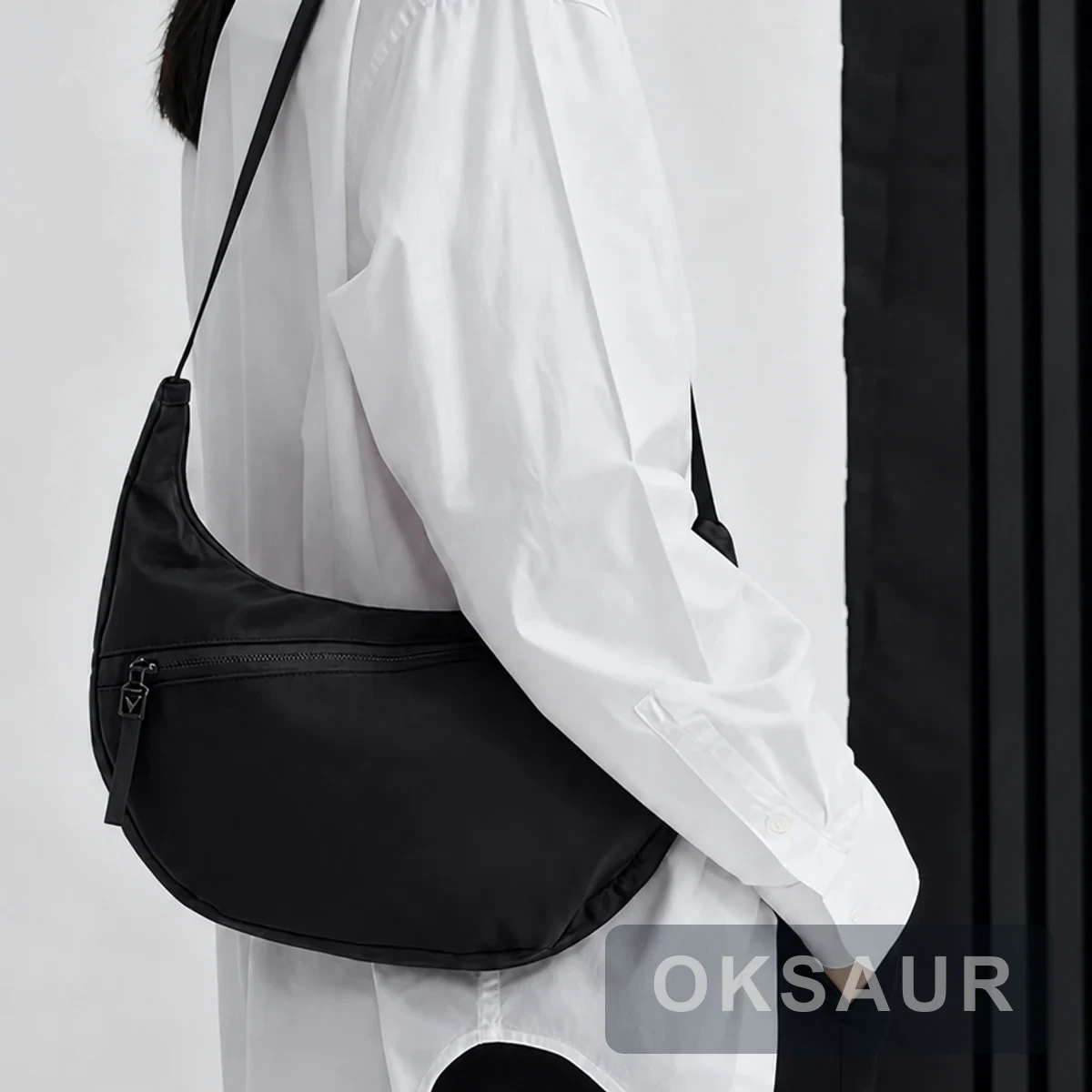 Black crescent crossbody bag worn across the body with an adjustable shoulder strap